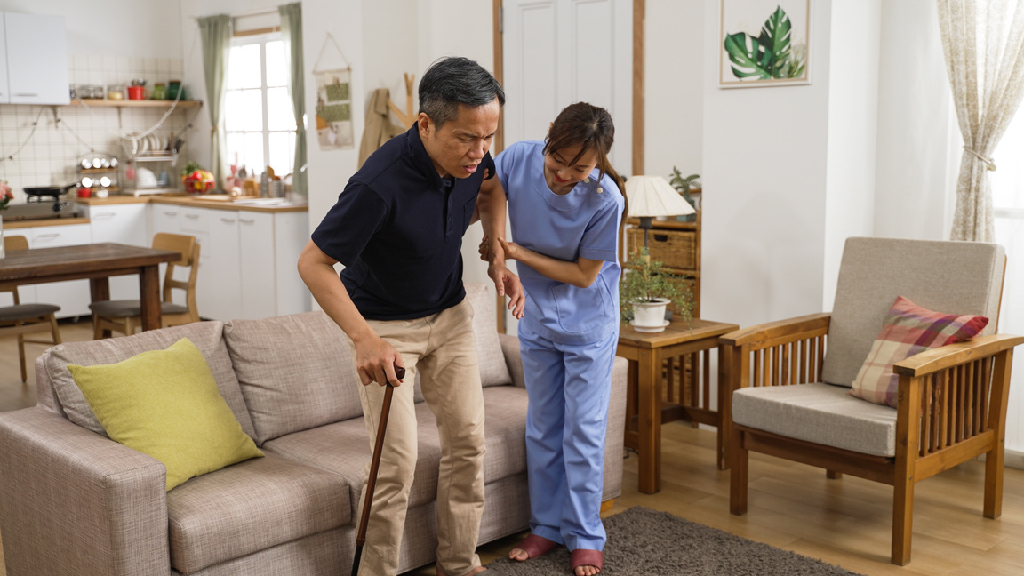 Korean Woman in-Home Care Attendant Assisting Senior Male to Sta